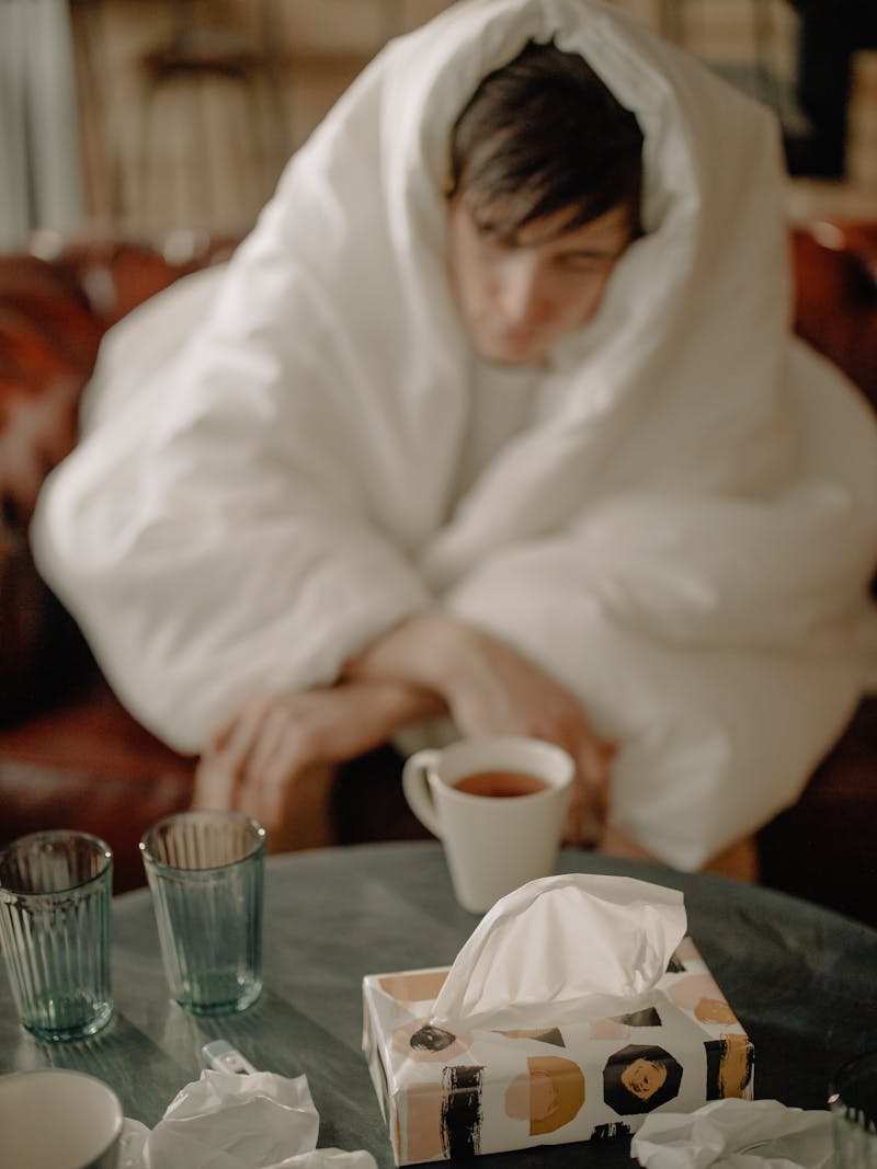 Person wrapped in blanket with tea and tissues — recovering from cold or flu at home