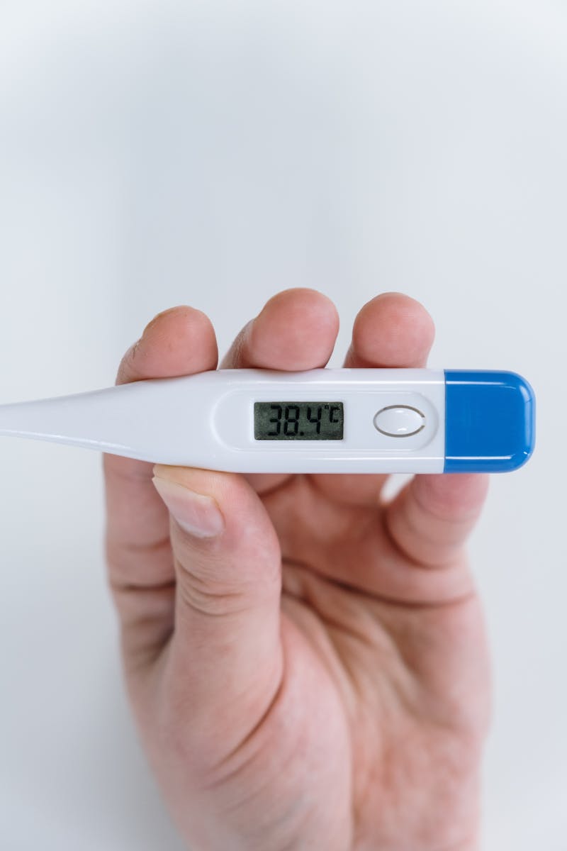 Digital thermometer showing 38.4°C fever — a key difference between cold and flu symptoms