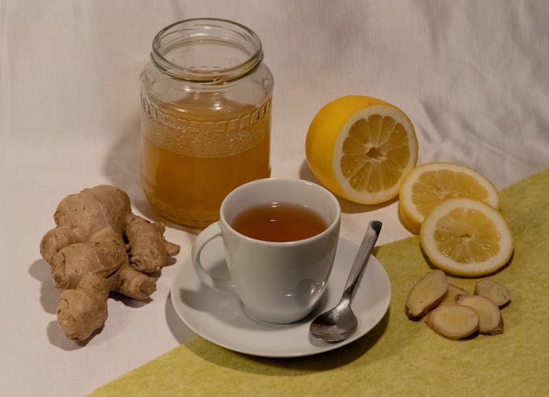 Fresh ginger root with a cup of ginger tea, honey jar, and lemon slices — natural cold remedy ingredients